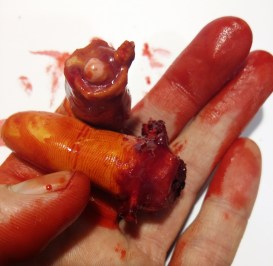 Mano sosteniendo simuladores de lesiones traumáticas con aspecto sangriento.